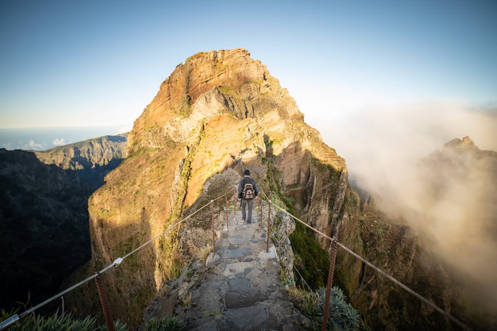 A lone hiker walks along a rugged mountain path at sunrise on Madeira Island.