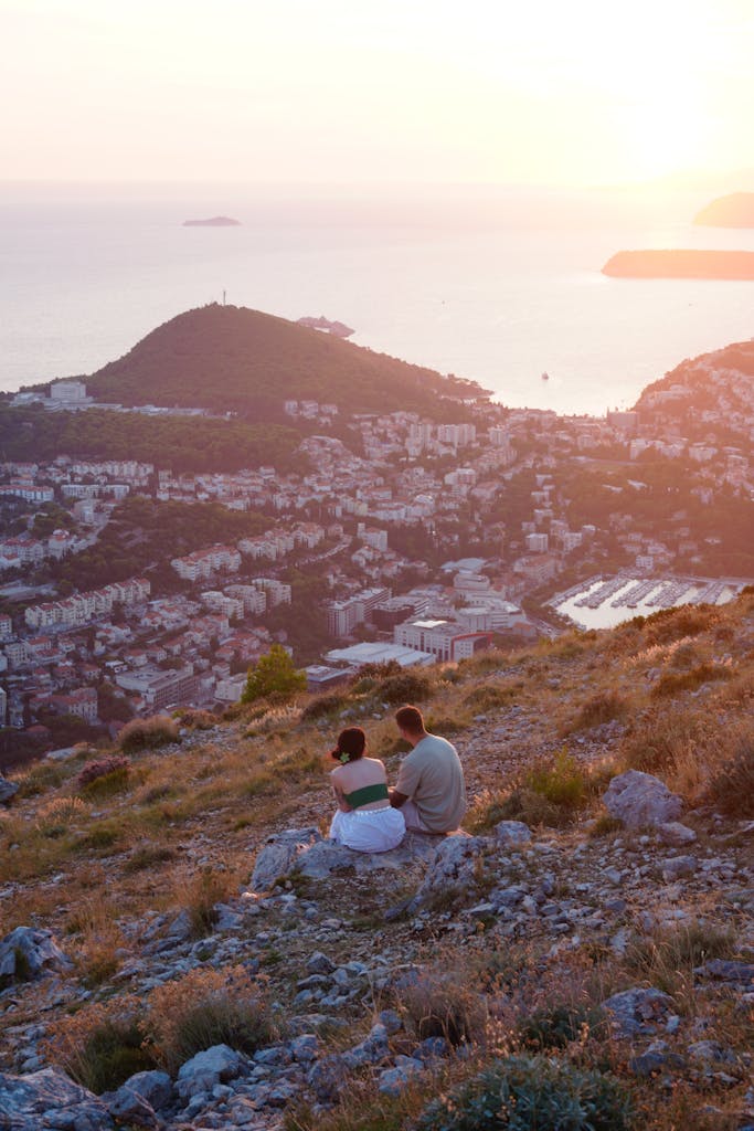 Couple sitting on a hill overlooking Dubrovnik coast at sunset, capturing a romantic moment.