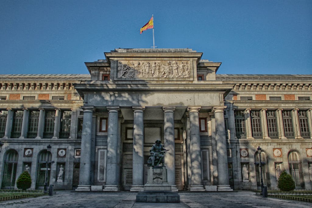 Exterior of the Prado Museum in Madrid with a clear blue sky and statue in front.