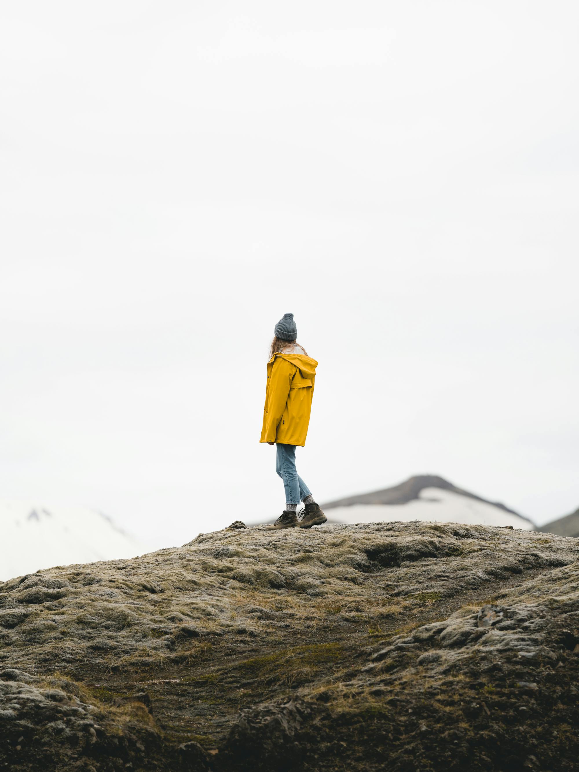Woman in yellow jacket hiking on mossy rocks in Iceland, embodying adventure and solitude.