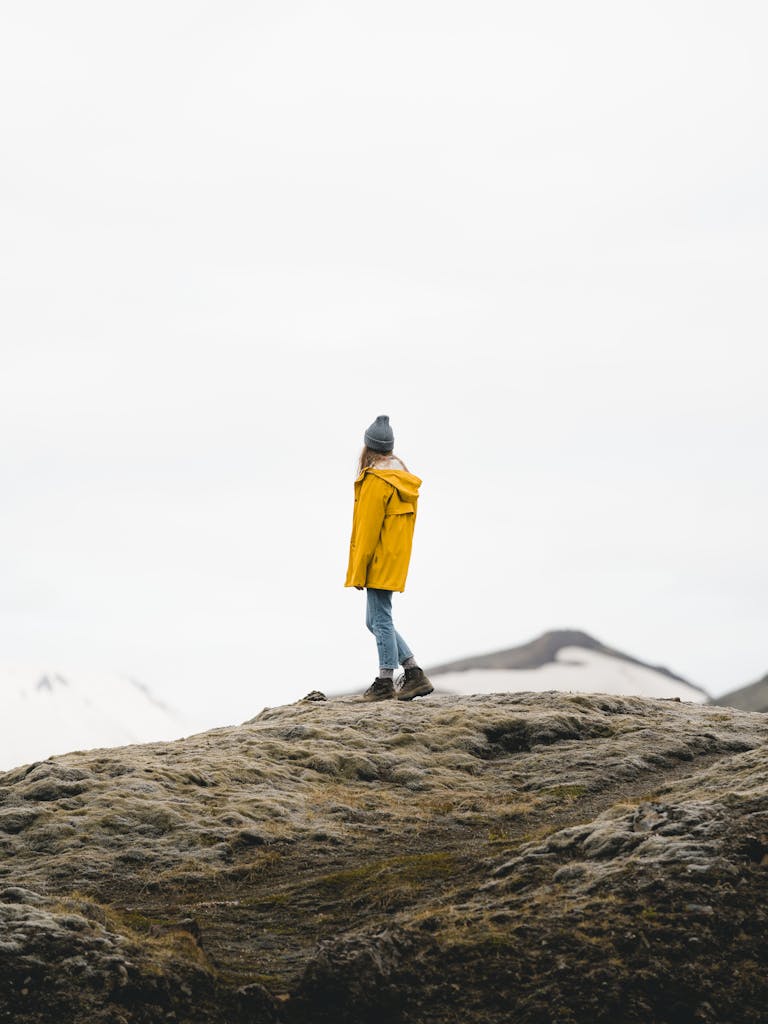 Woman in yellow jacket hiking on mossy rocks in Iceland, embodying adventure and solitude.